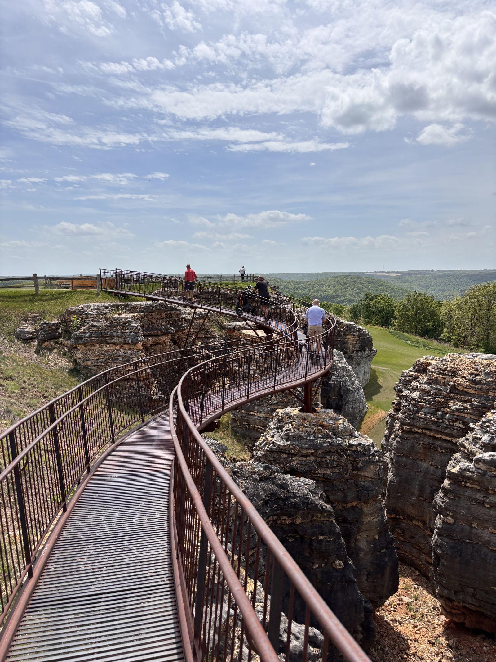 The clifftop walkway winding over rugged rock formations at Top of the Rock, with the golf course and Ozark hills beyond